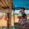 african street vendor, mother holding her child between the bags of cabbage and tomatoes in the shed